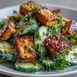 Freshly sliced cucumbers and crunchy carrots are tossed in a creamy sesame-ginger dressing, topped with ultra-crispy tofu for this vibrant salad. 