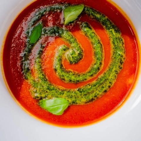 Velvety Tomato Soup with Basil Pesto Swirl steaming in a rustic bowl, the vibrant green swirl contrasting with the rich red.