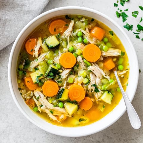 Steaming pot of Spring Garden Chicken Soup on a rustic kitchen counter, garnished with fresh parsley and a lemon wedge for extra brightness. 