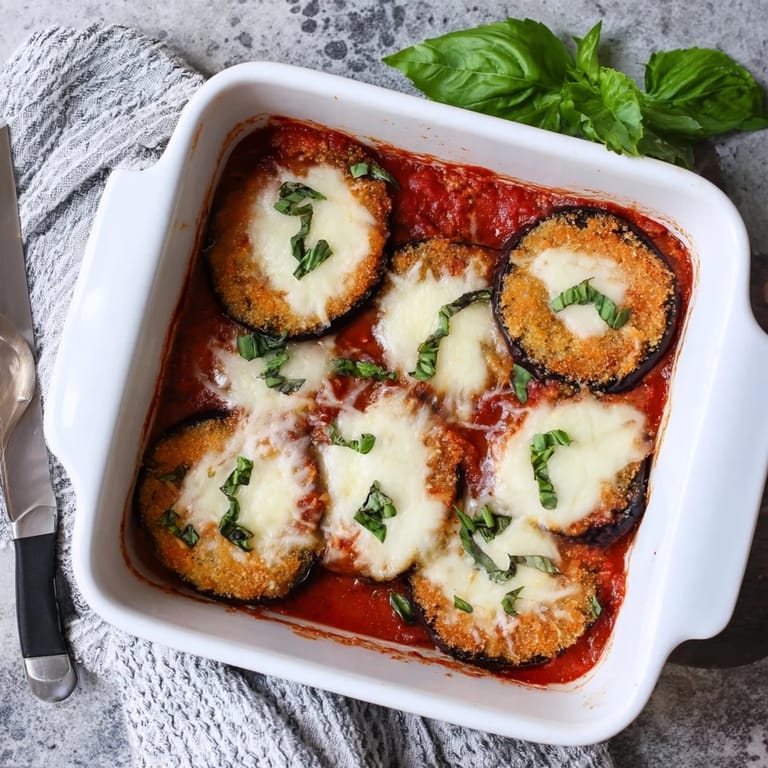 Serving of cheesy Eggplant Parmesan on a white plate, ready to enjoy with a side salad.
