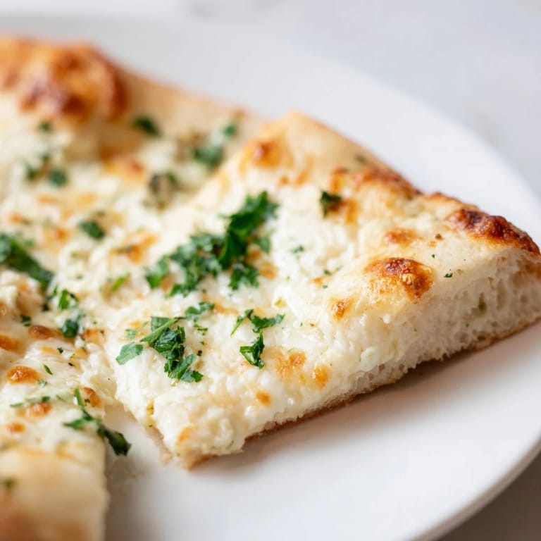 Freshly sliced creamy garlic white pizza with visible garlic cream sauce on a rustic kitchen counter.