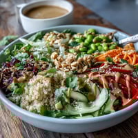 Freshly prepared Thai Coconut Quinoa Bowl with vibrant red peppers, shredded carrots, and cucumber, drizzled with creamy peanut dressing and garnished with cilantro.